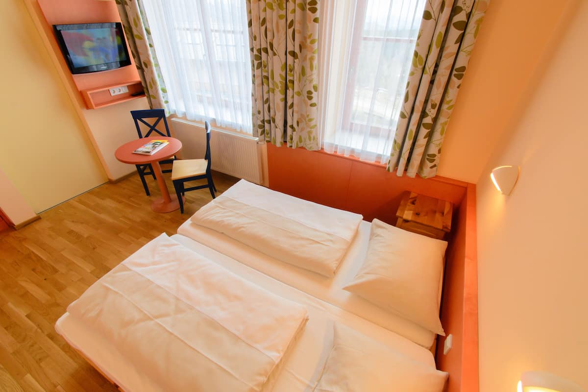 Habitación de hotel con dos camas, una mesita con una silla, televisión y ventana con cortinas.
