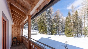 A wooden balcony with a view of a snowy landscape and trees. -  JUFA Hotel Hochrindl (Albeck)
