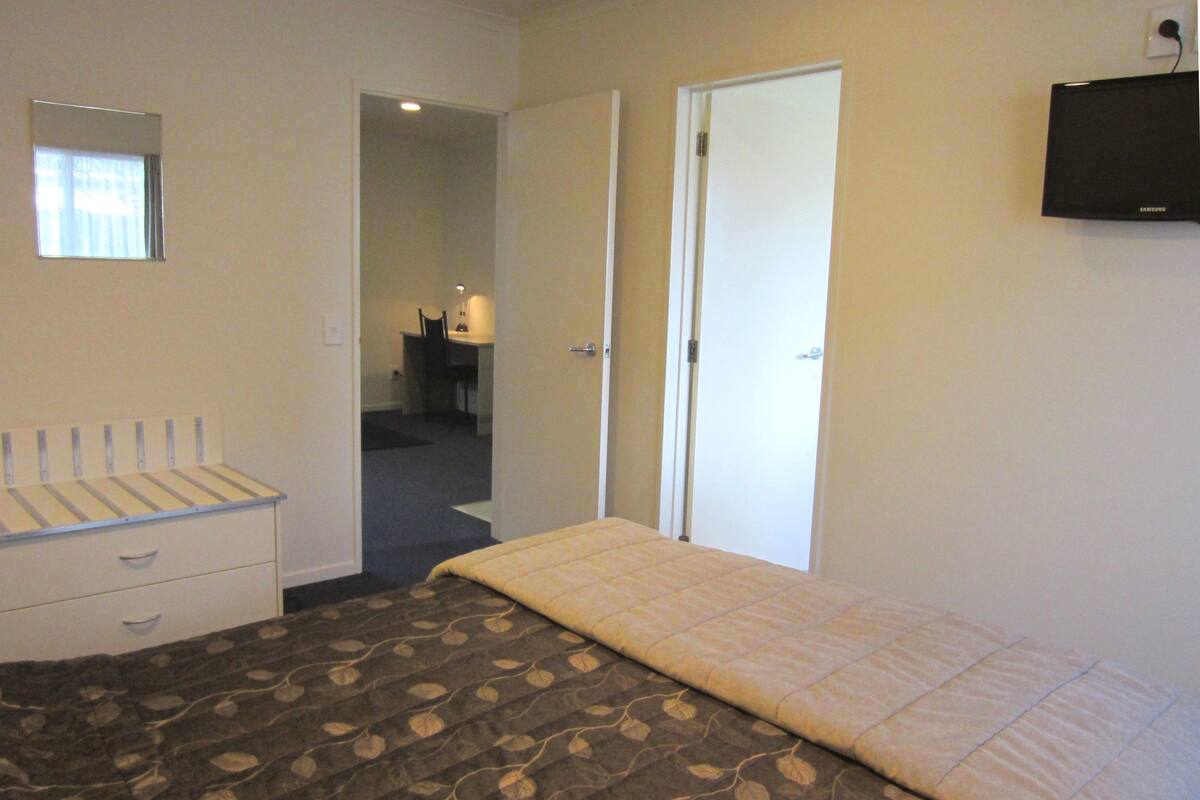 Un dormitorio con cama, cómoda, televisor y puerta que da a otra habitación.