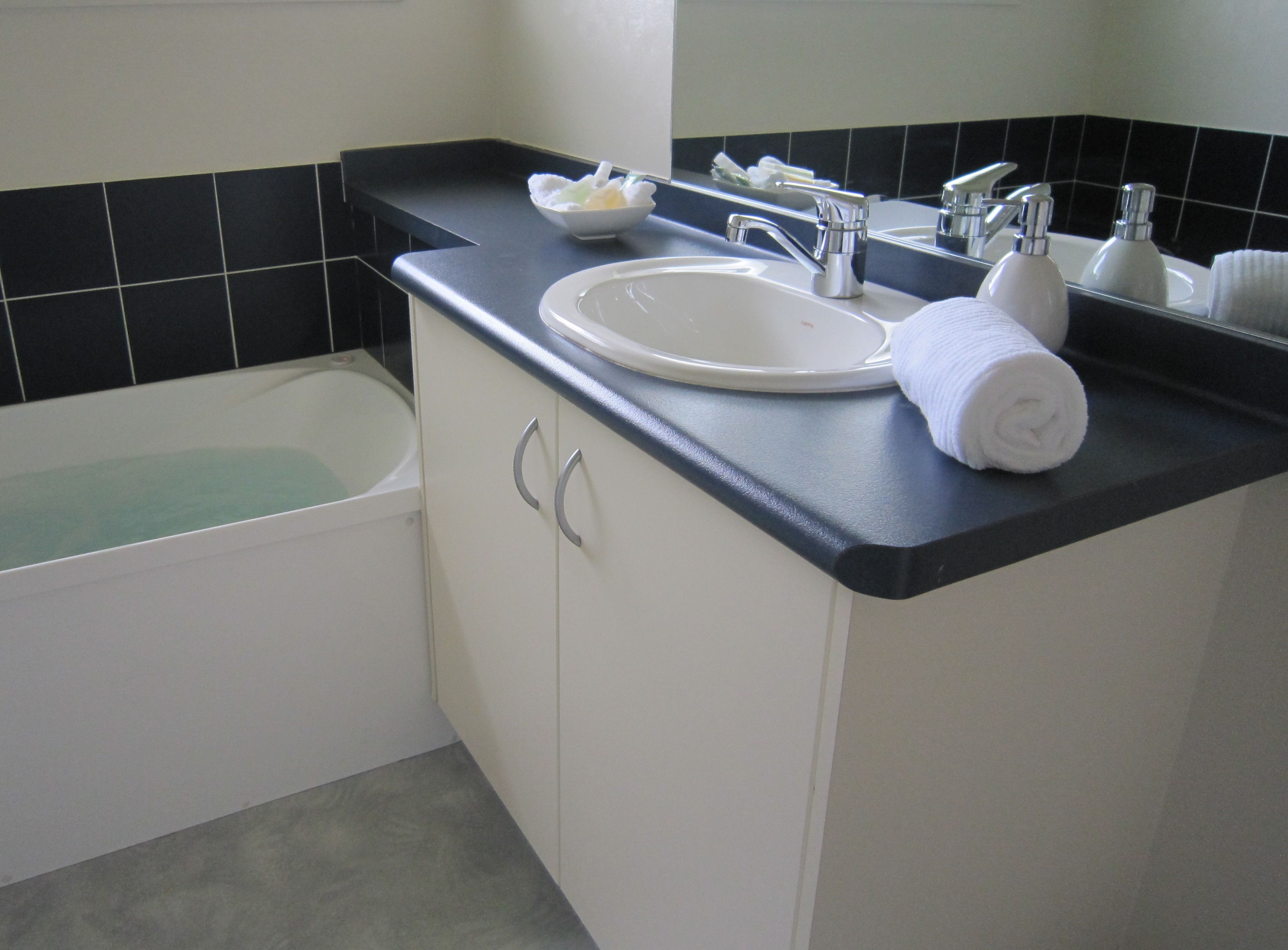 A bathroom with a white sink, black countertop, and a white bathtub.