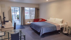 Een hotelkamer met een bed, een bureau met stoel, een klein tafeltje en een raam met gordijnen.