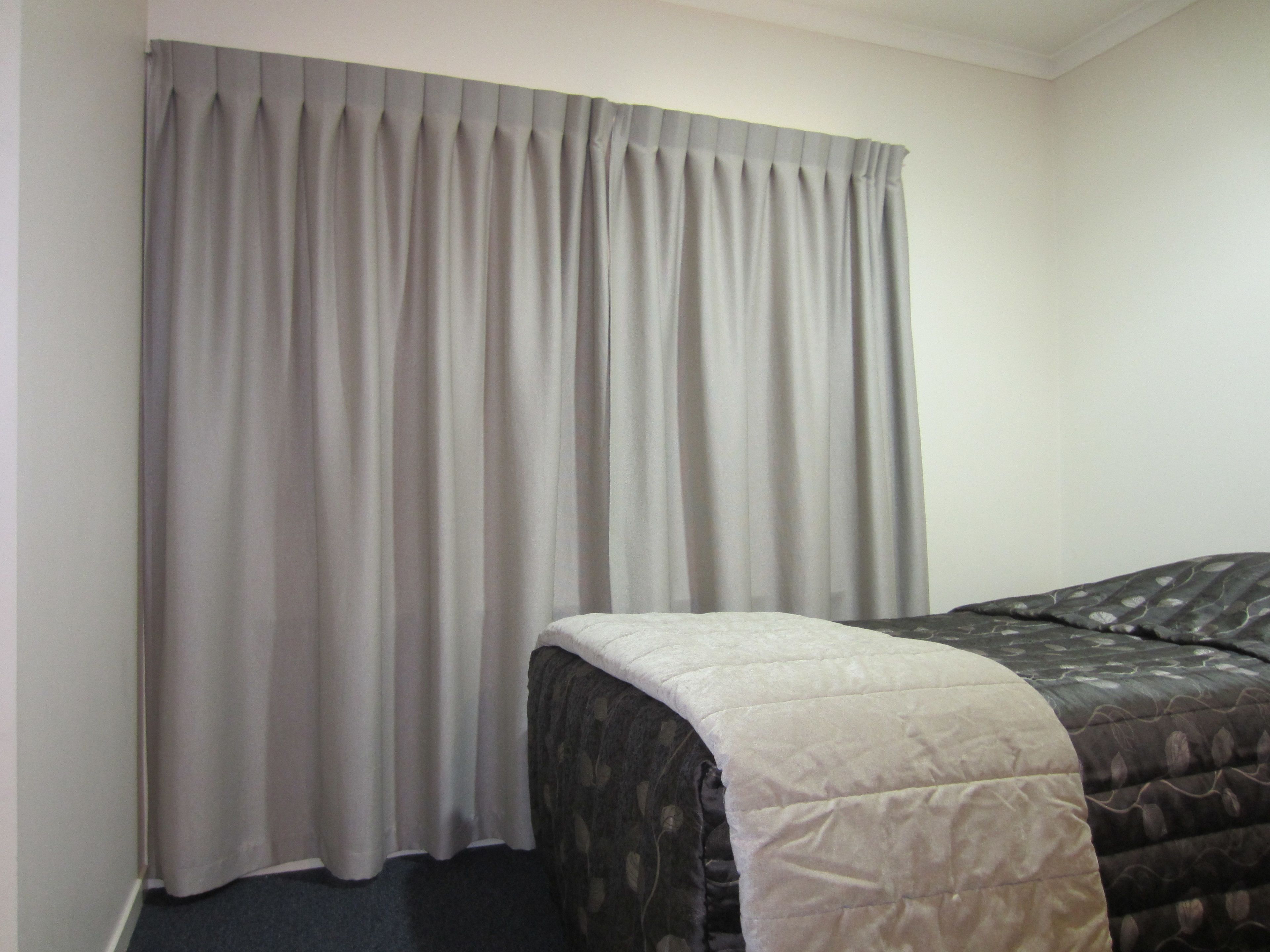 A hotel room with a bed, a grey curtain, and a carpeted floor.