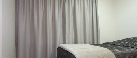 A hotel room with a bed, a grey curtain, and a carpeted floor.