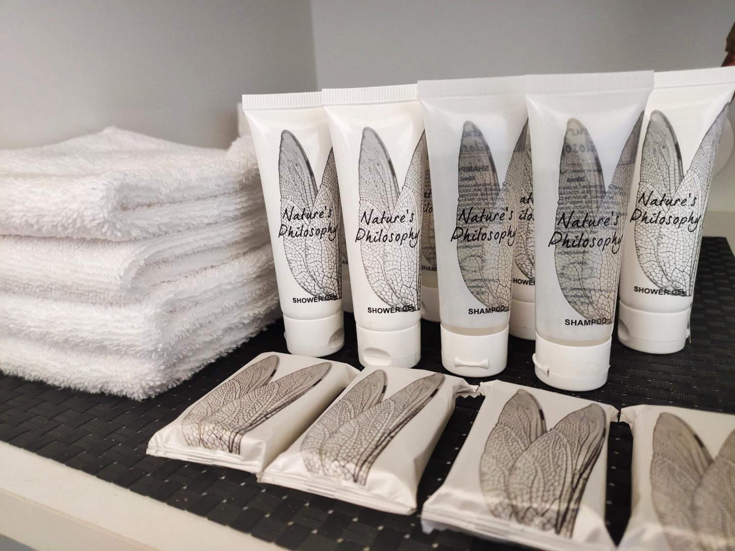 Se exhiben botellas de gel de ducha y champú de Nature’s Philosophy, junto con toallas blancas dobladas con cuidado.