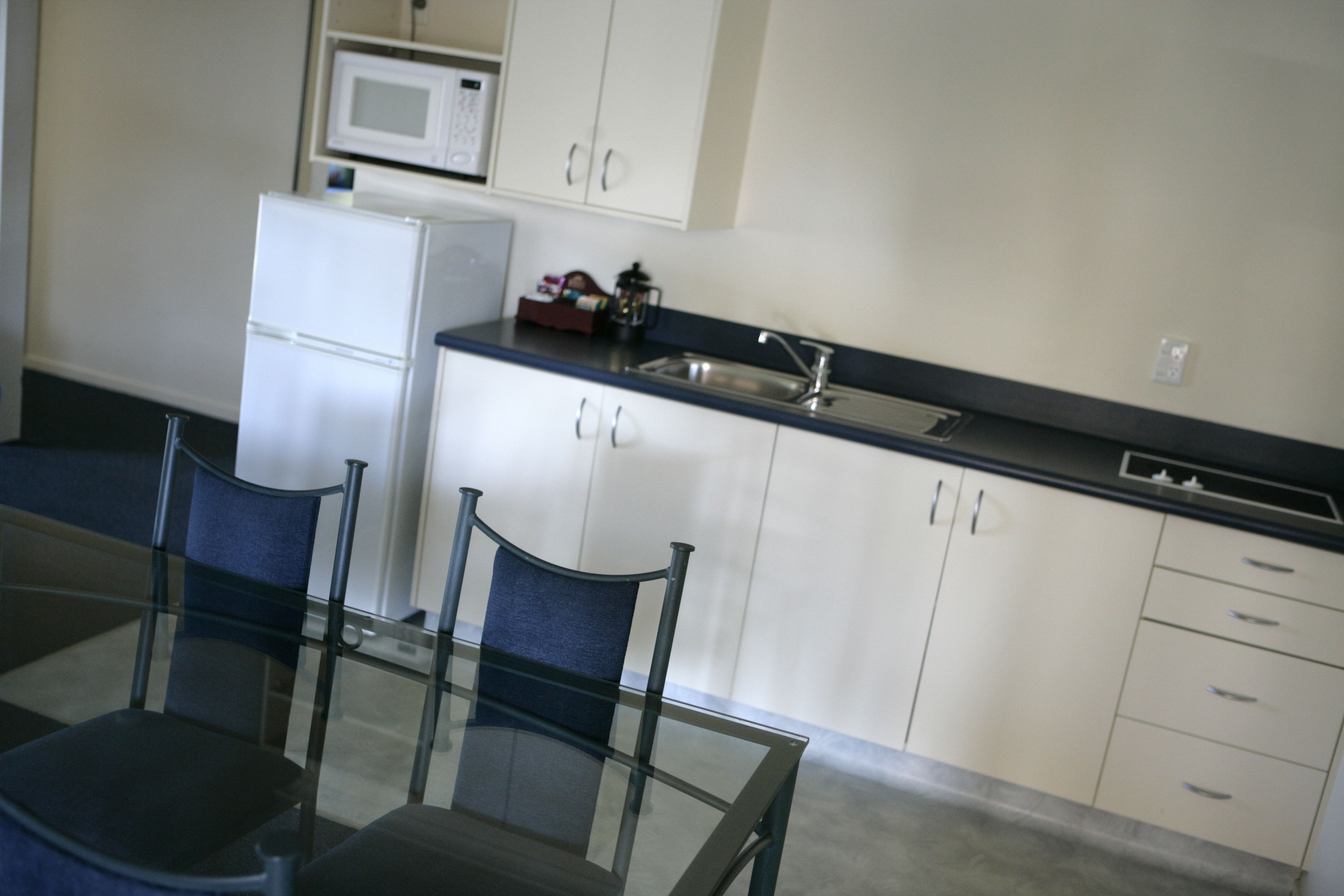 A modern kitchen with white cabinets, a black countertop, and a glass dining table with chairs.
