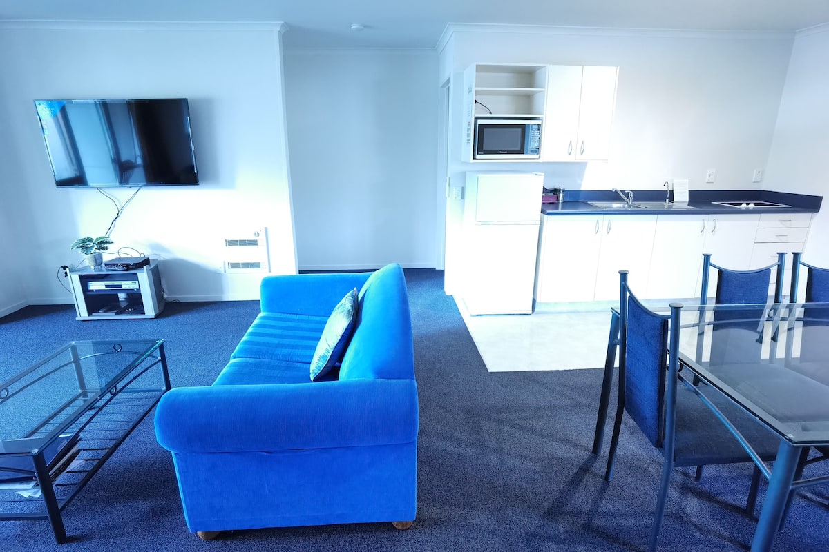 Una sala de estar moderna con un sofá azul, una mesa de centro de vidrio y un televisor de pantalla plana montado en la pared.
