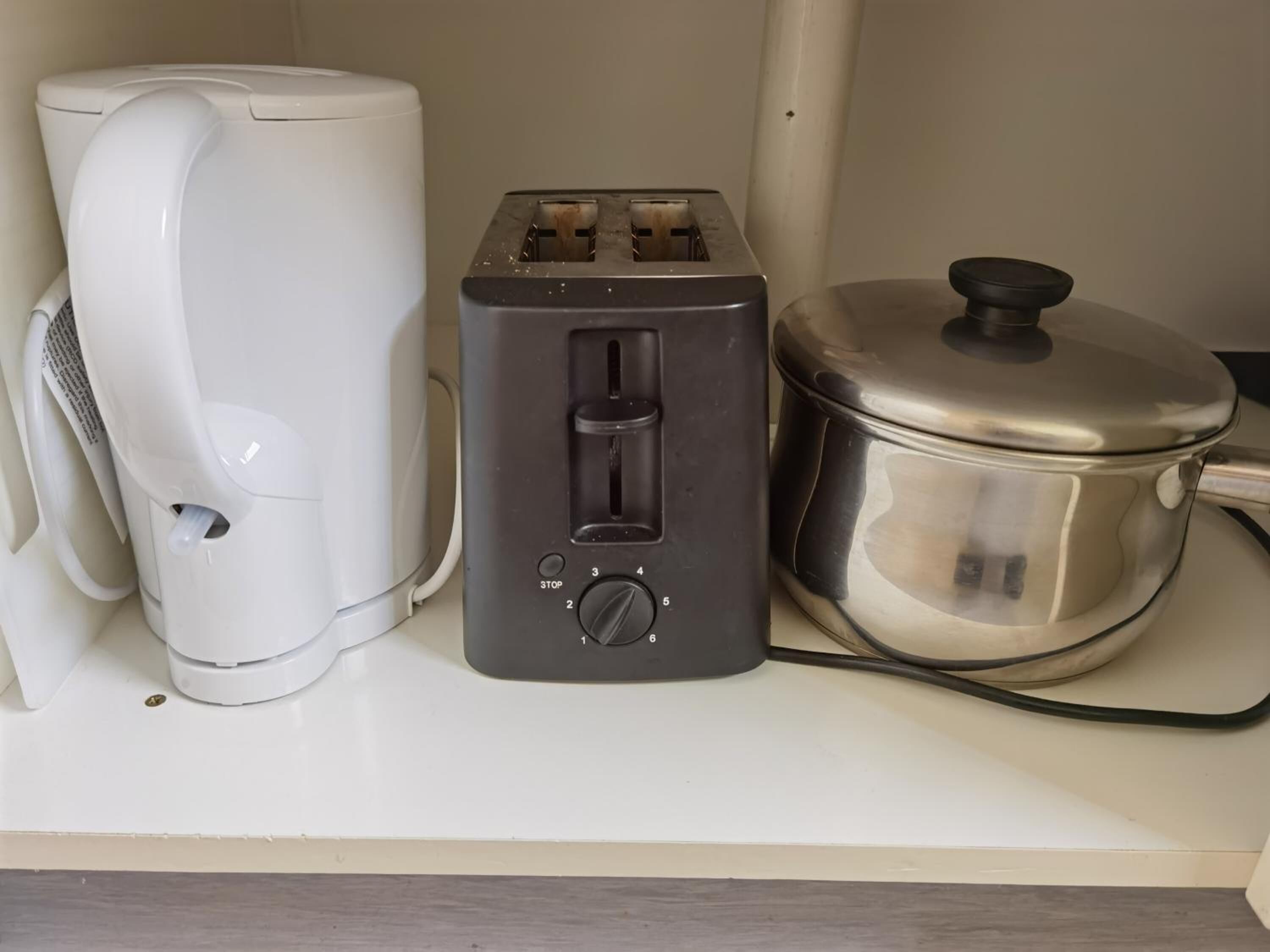 A kitchen with a white toaster, a black electric kettle, and a stainless steel pot on a countertop.