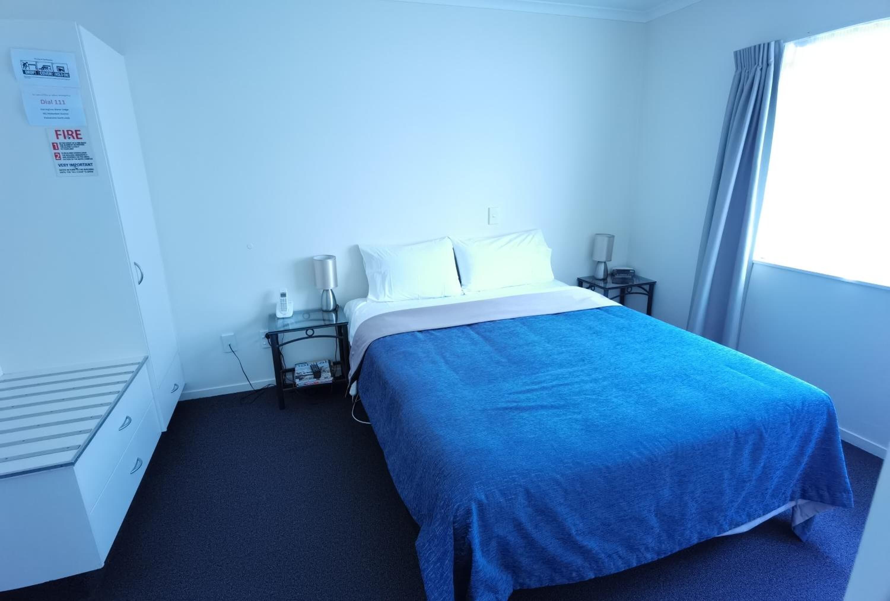 Habitación de hotel con cama, escritorio, silla, armario y ventana con cortinas.