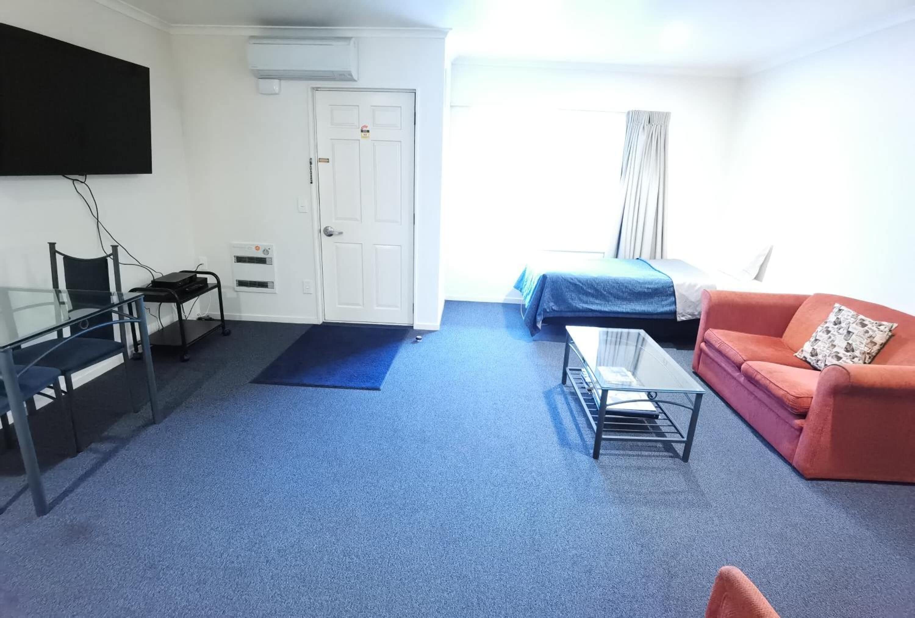Une pièce comprenant un lit, un canapé, un bureau avec une chaise et un téléviseur fixé au mur.