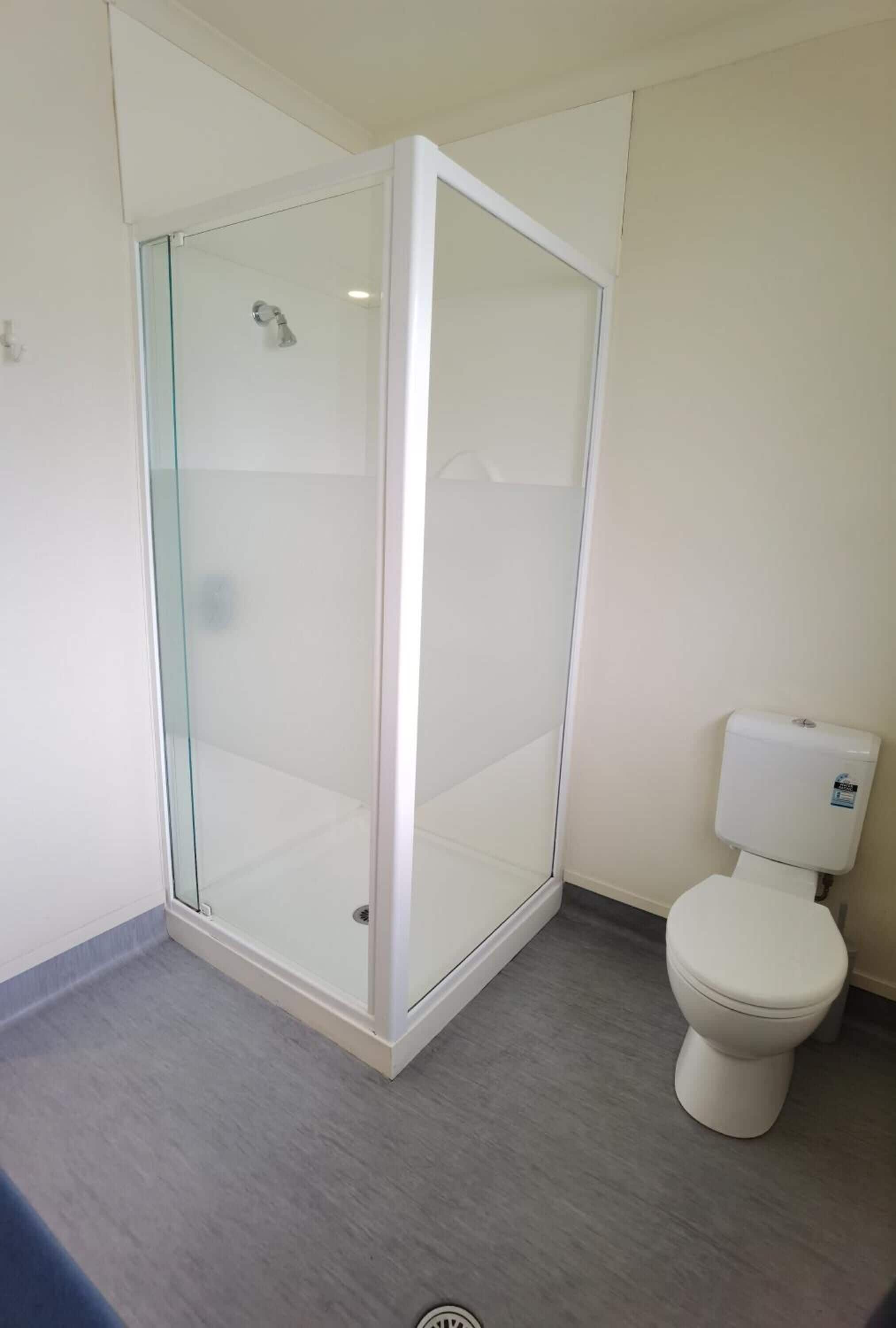 A bathroom with a glass-enclosed shower, a toilet, and a grey floor.