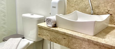 A bathroom with a toilet, a sink, a paper towel dispenser, and a shower.