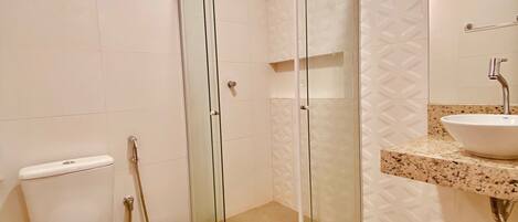 Un baño moderno con cabina de ducha de vidrio, inodoro y lavabo con encimera de mármol.