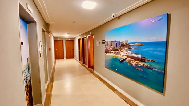 A hotel hallway with a large painting of a coastal cityscape, multiple doors, and a tiled floor.