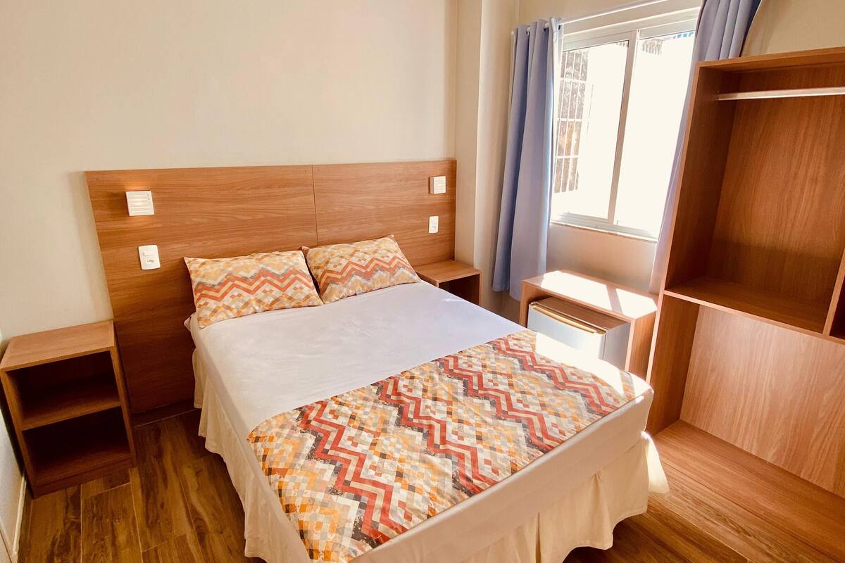 A neatly arranged bedroom with a wooden bed, a nightstand, a wardrobe, and an air conditioning unit.