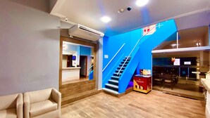 A hotel lobby with a reception desk, a staircase, and a seating area.