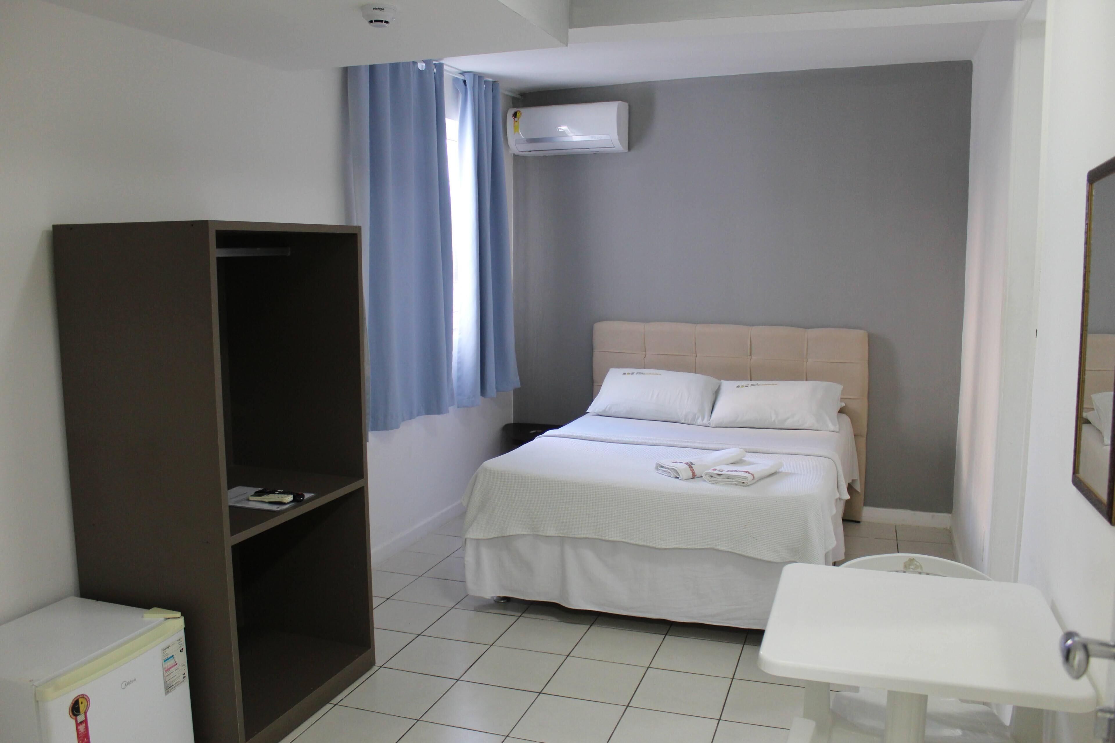 A hotel room with a bed, a wardrobe, a small desk, a sink, and an air conditioning unit.