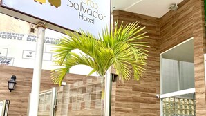 A hotel entrance with a sign reading "Porto Salvador Hotel," a potted palm tree, and a tiled floor.