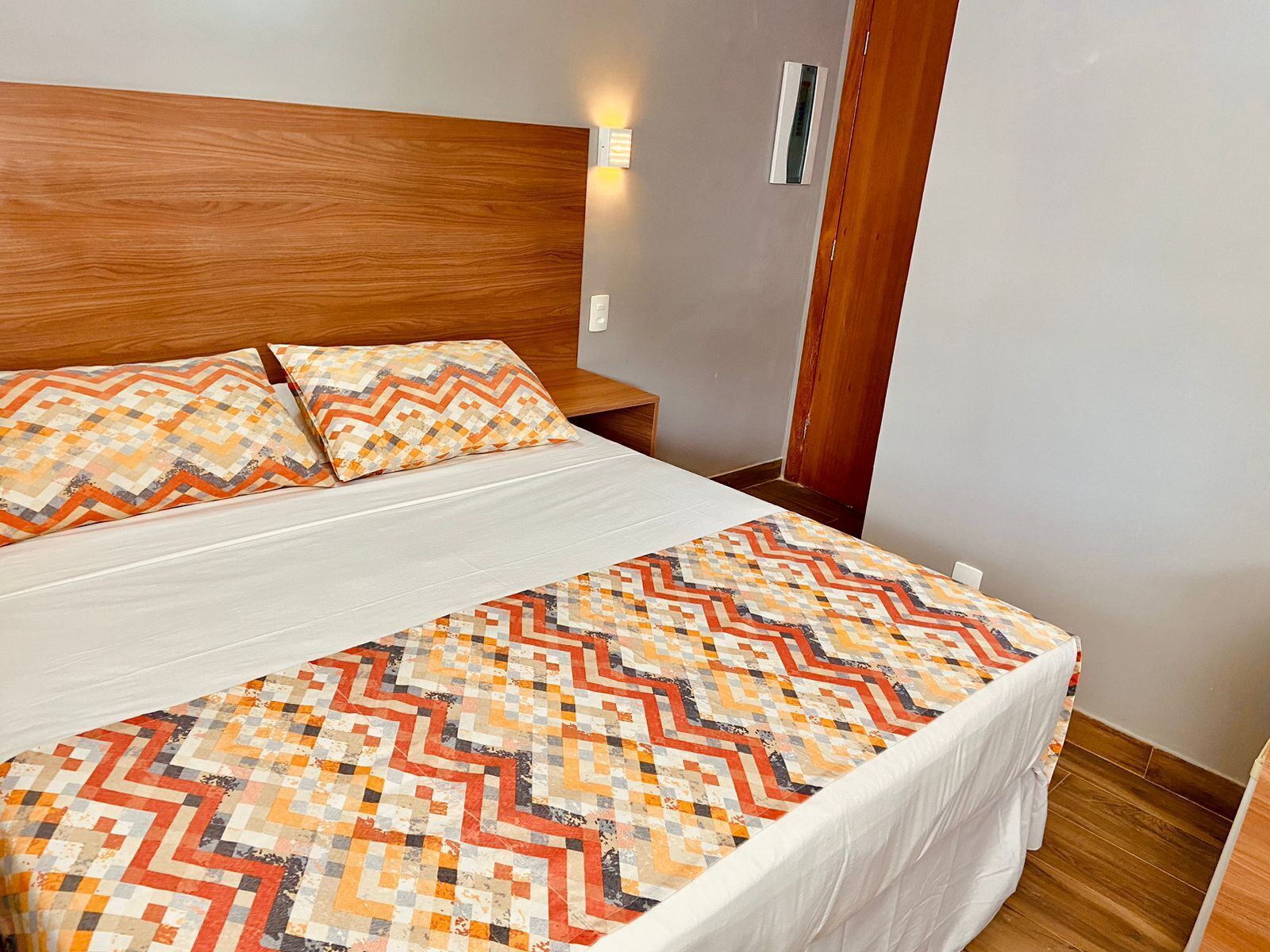 A neatly made bed with patterned bedding, a wooden headboard, and a bedside table with a lamp.