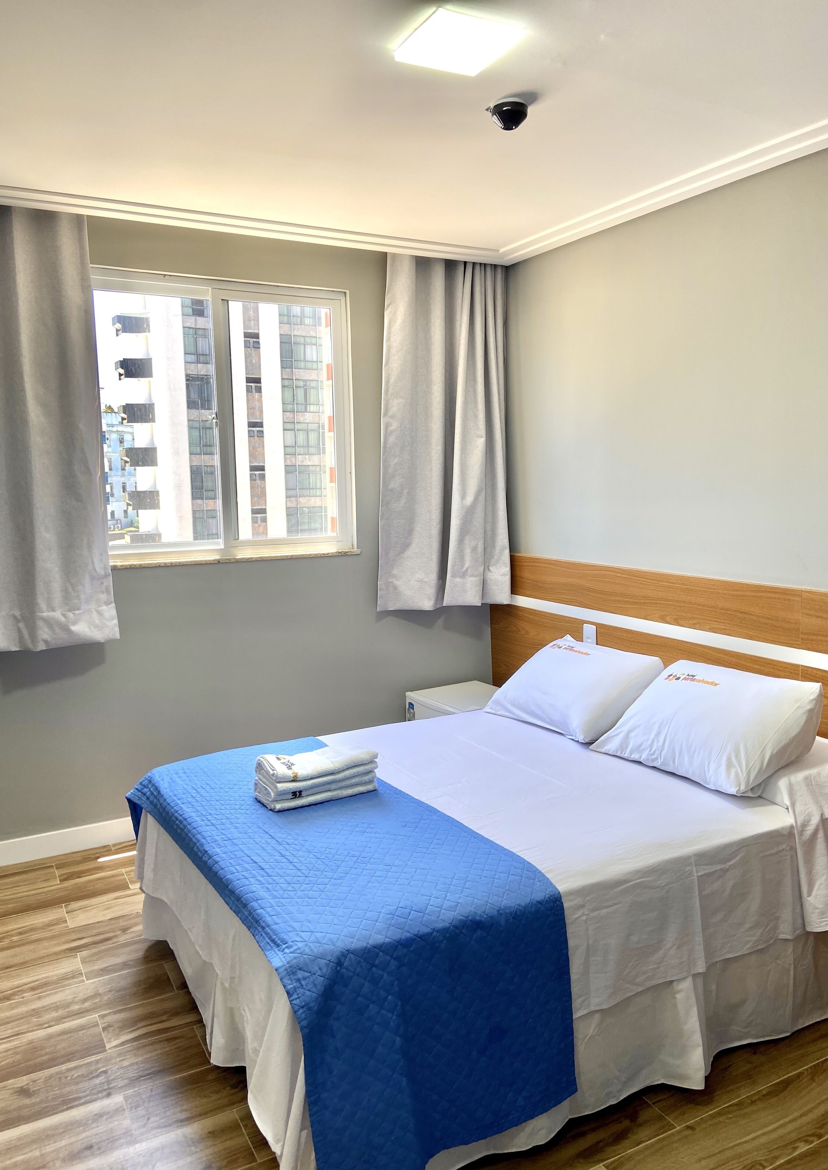 Ein ordentlich bezogenes Bett mit einer blau-weißen Tagesdecke, einem hölzernen Kopfteil und einem Fenster mit Vorhängen.