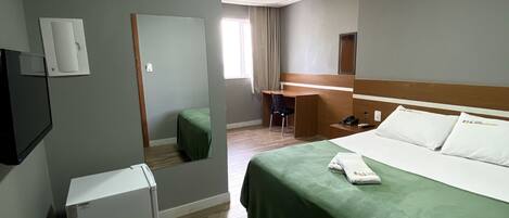 A hotel room with a bed, a small refrigerator, a desk, and a mirror.