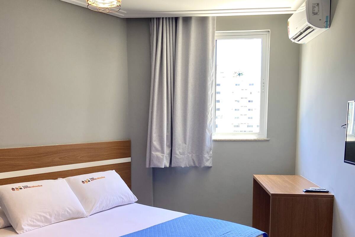 A neatly made bed with a blue quilt, a wooden headboard, and a hanging light fixture.