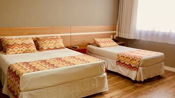 A hotel room with two beds, wooden flooring, and a window with curtains.
