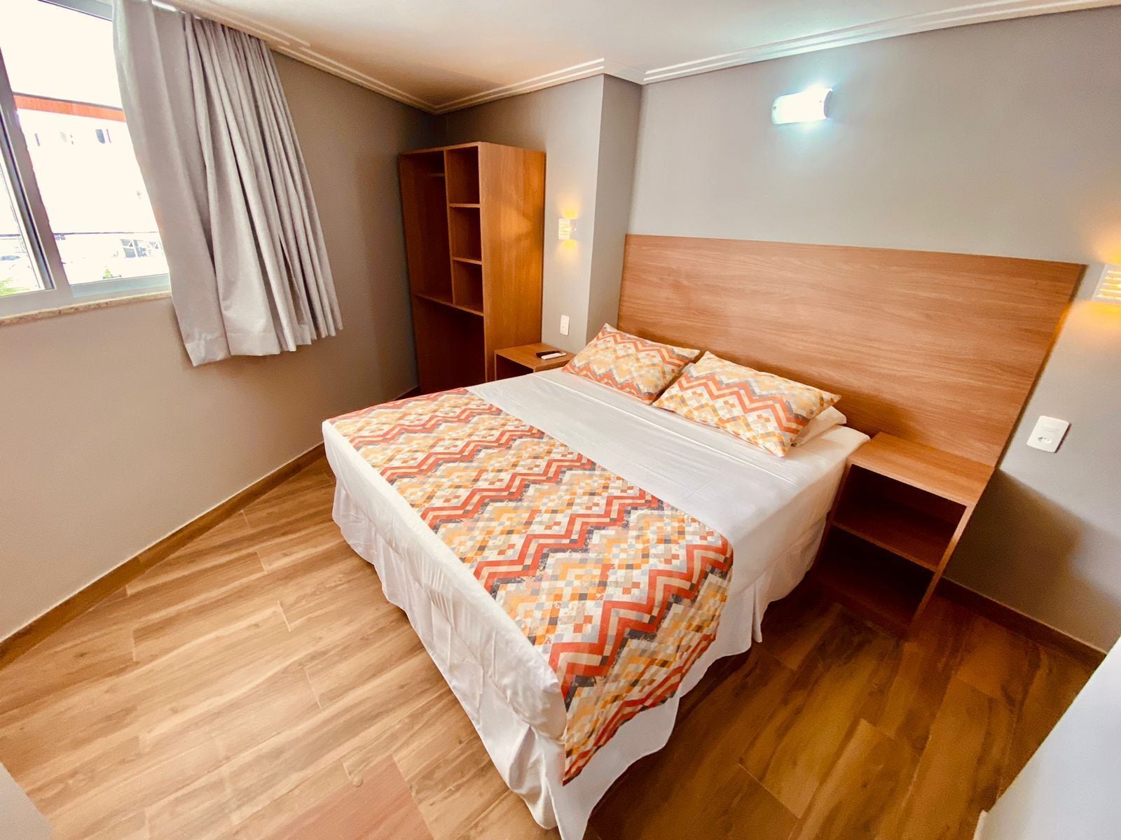 Une chambre d’hôtel avec un grand lit, une tête de lit en bois et une armoire intégrée.