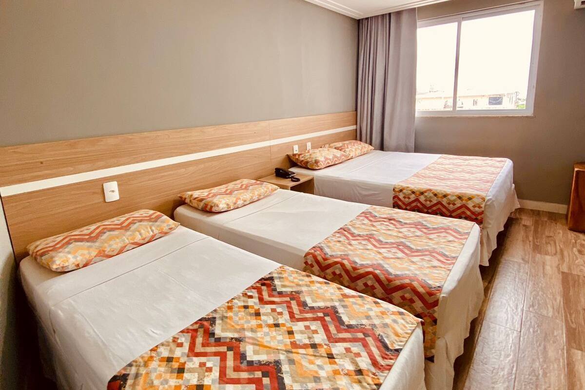 A hotel room with three single beds, a wooden headboard, a window with curtains, and a wooden floor.