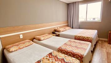 Habitación de hotel con tres camas individuales, cabecera de madera, ventana con cortinas y suelo de madera.