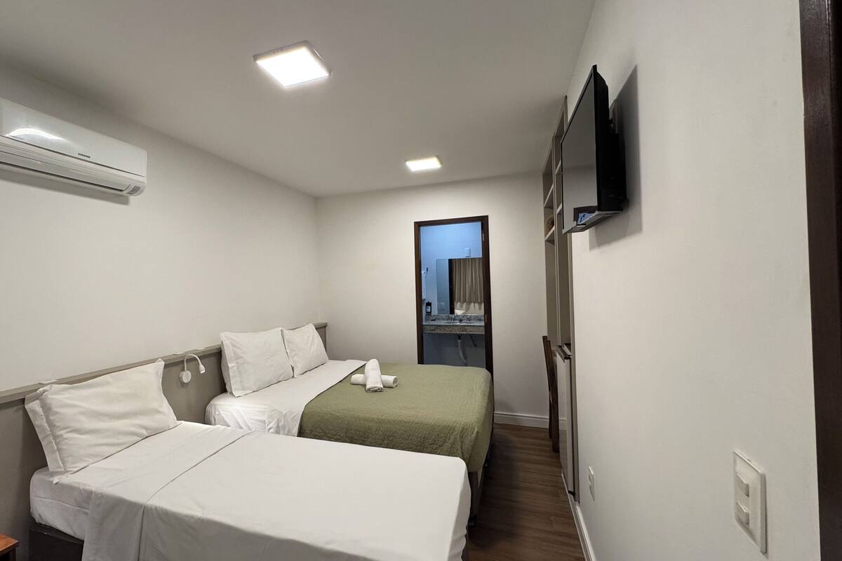 Een hotelkamer met twee bedden, een flatscreen televisie, een airconditioner en een klein nachtkastje.