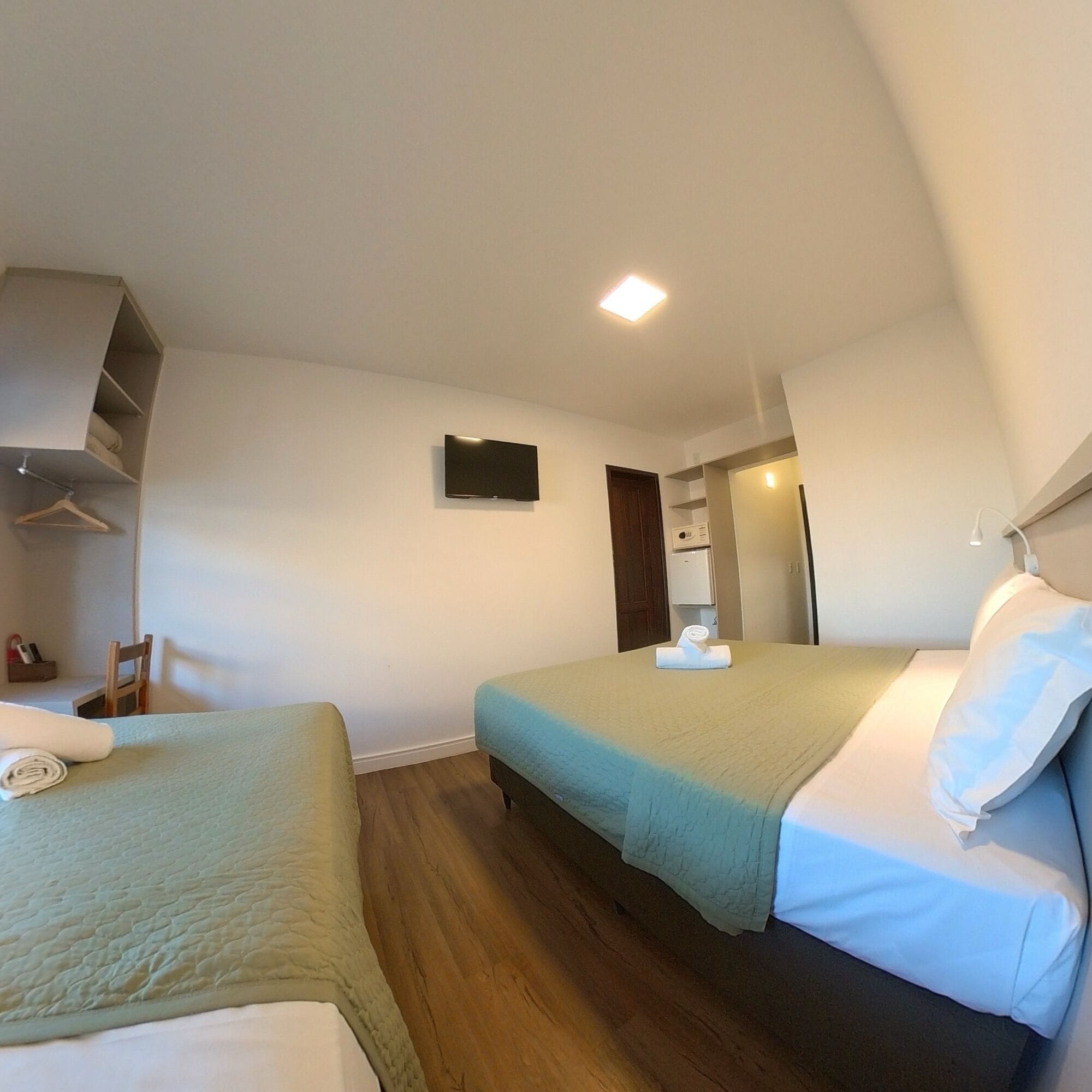 Quarto de hotel com duas camas, televisão presa na parede e piso de madeira.