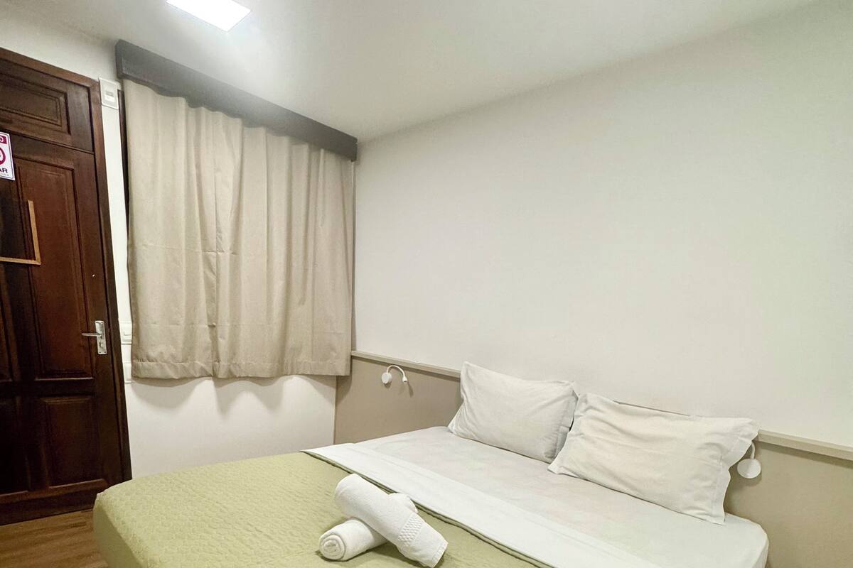 Een netjes opgemaakt bed met een groene plaid, een wit kussen en een opgerolde witte handdoek op het bed.