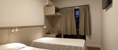 A hotel room with two beds, a ceiling light, a TV mounted on the wall, and a window with curtains.