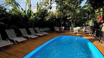 A swimming pool with lounge chairs and a wooden deck, surrounded by lush greenery and trees.