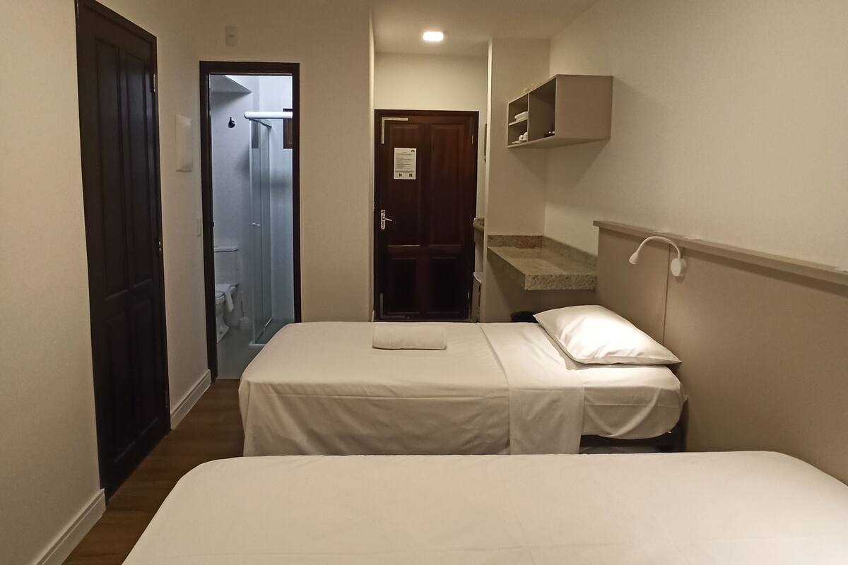Een hotelkamer met een eenpersoonsbed, een klein nachtkastje, een nachttafeltje, een inbouwplank en een deur naar een badkamer.