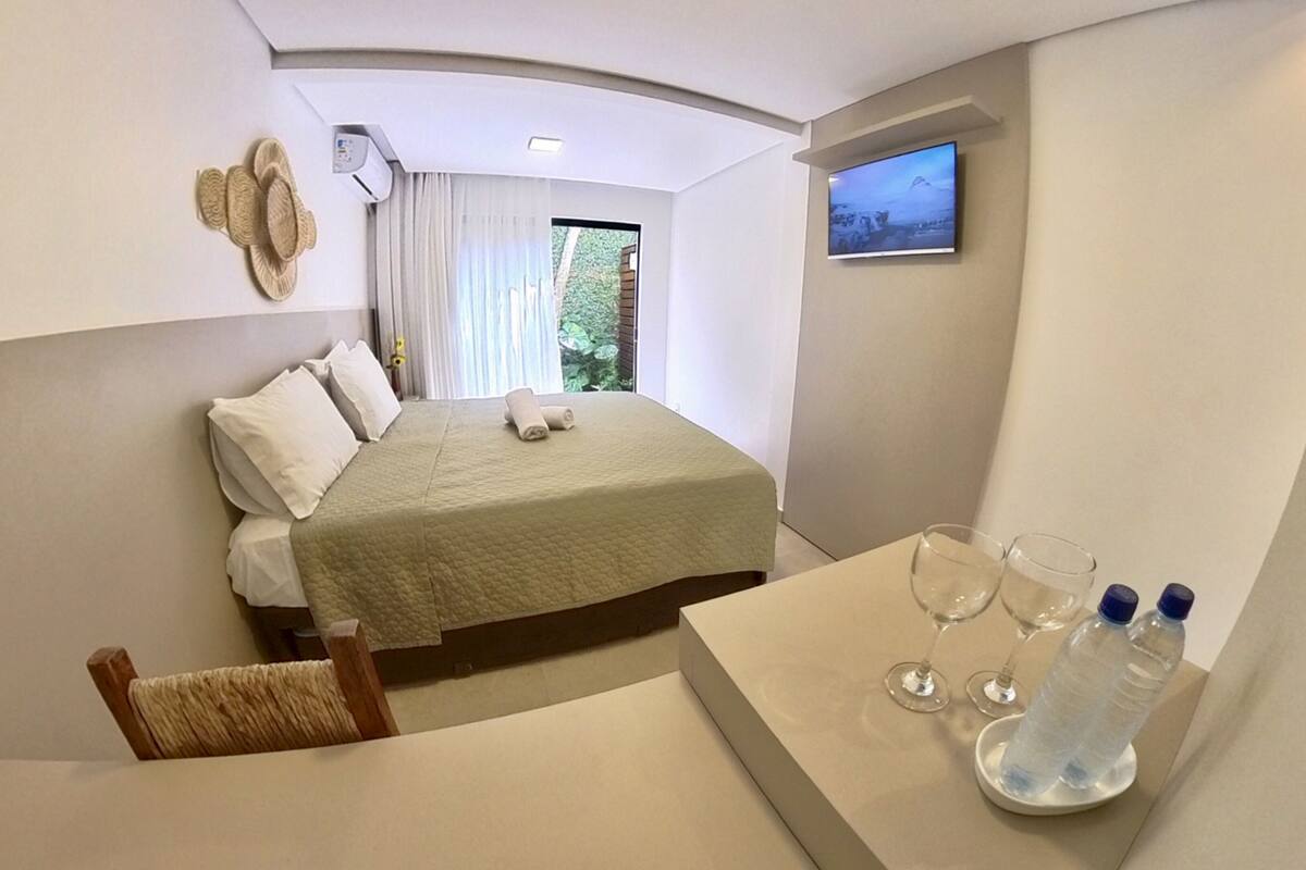 Hotelkamer met een bed, een tafeltje met glazen en waterflesjes, een televisie en een raam met gordijnen.