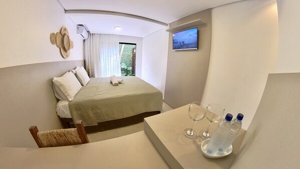 Habitación de hotel con cama, una mesita con vasos y botellas de agua, televisión y ventana con cortinas.
