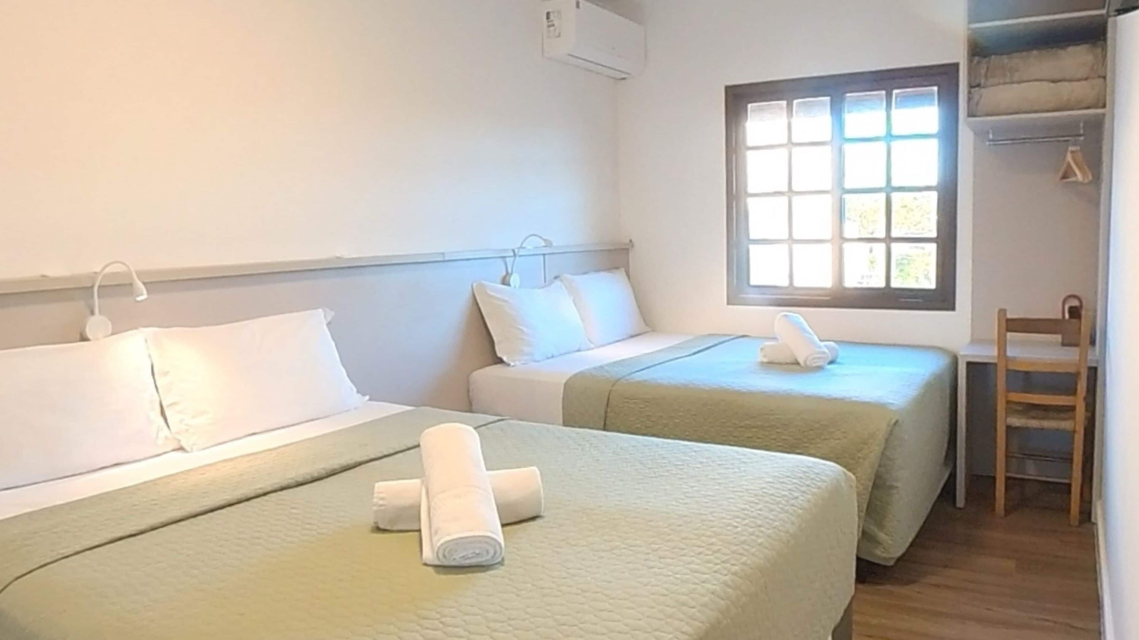 A hotel room with two beds, a window with blinds, a desk, and a chair.