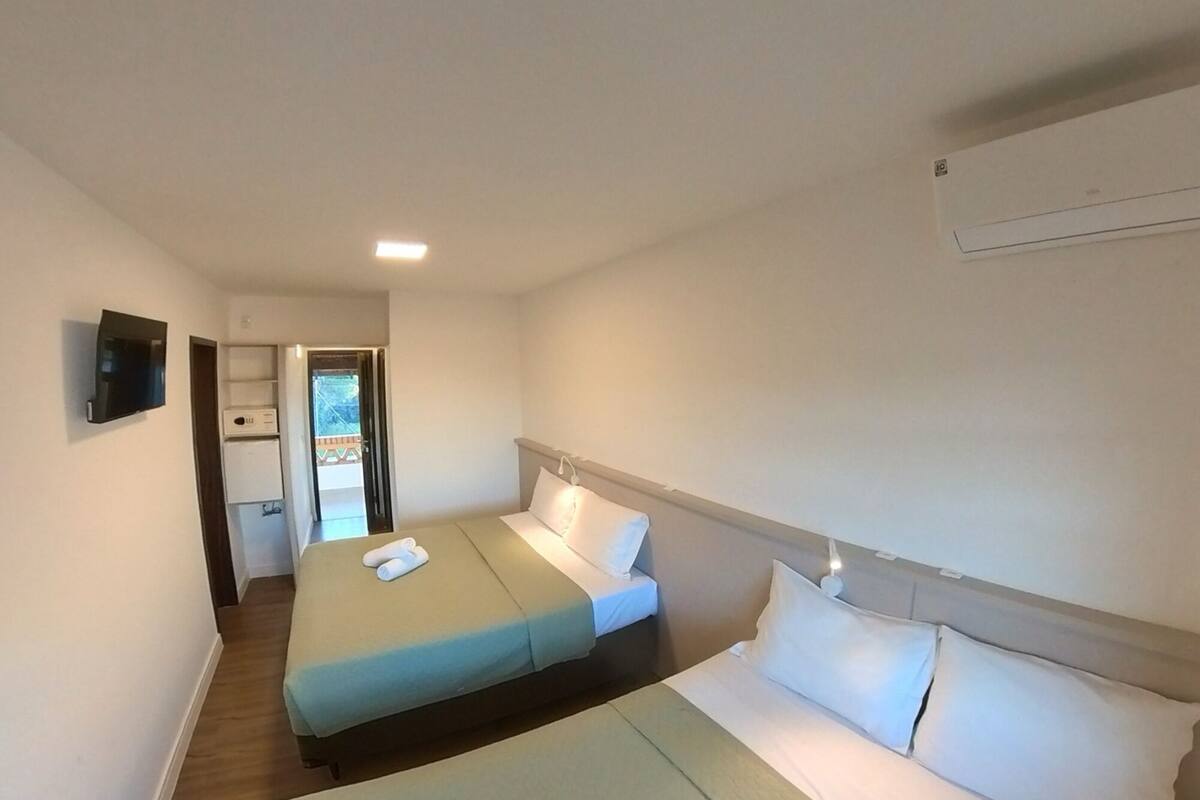 Een hotelkamer met twee bedden, een aan de muur bevestigde televisie en een deur naar een balkon.