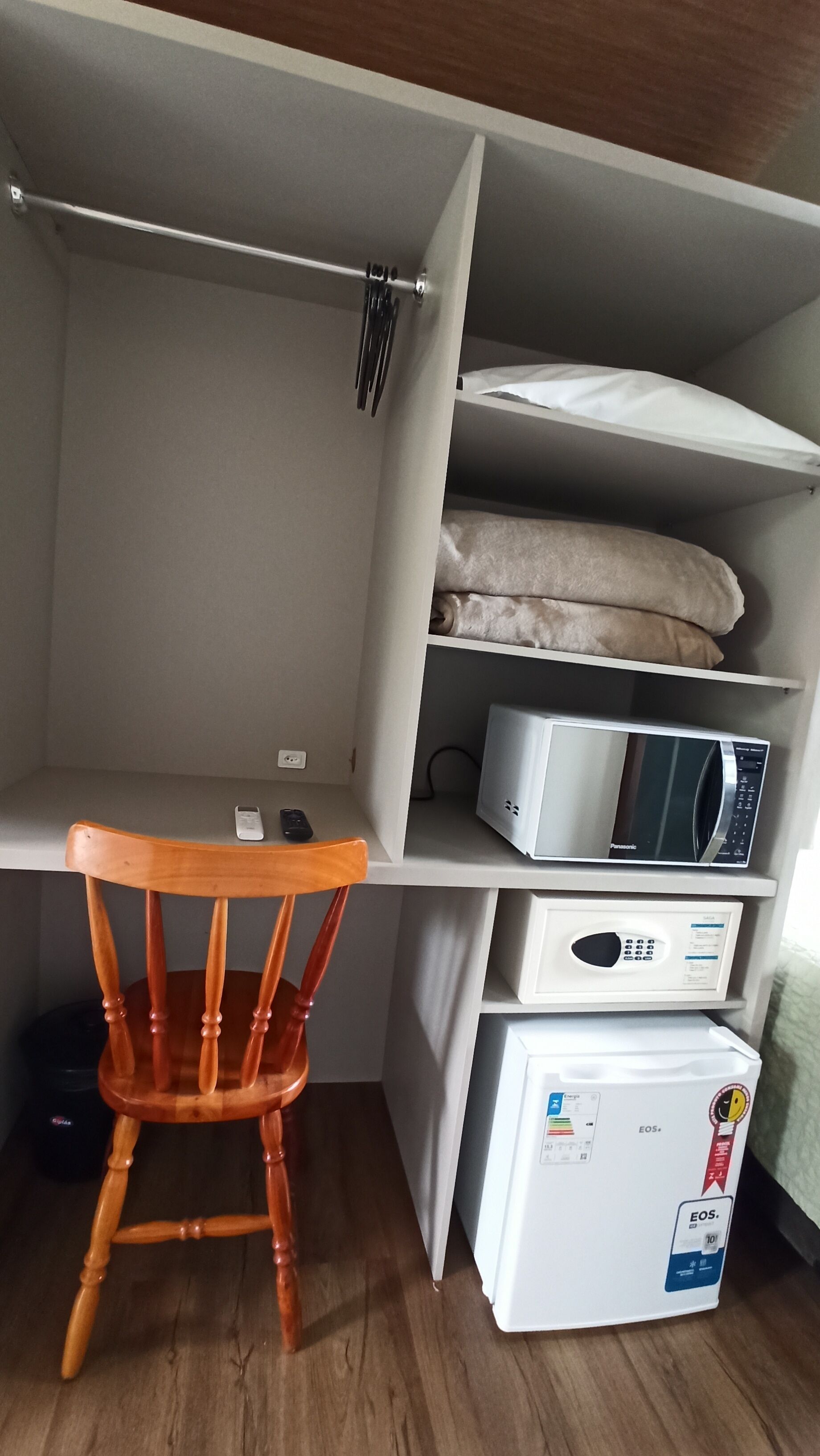 Una habitación pequeña con una silla de madera, microondas y refrigerador.