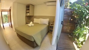 A bedroom with a bed, a bedside table, a wardrobe, and a view of greenery outside. - Hotel Natur Campeche (Florianópolis)