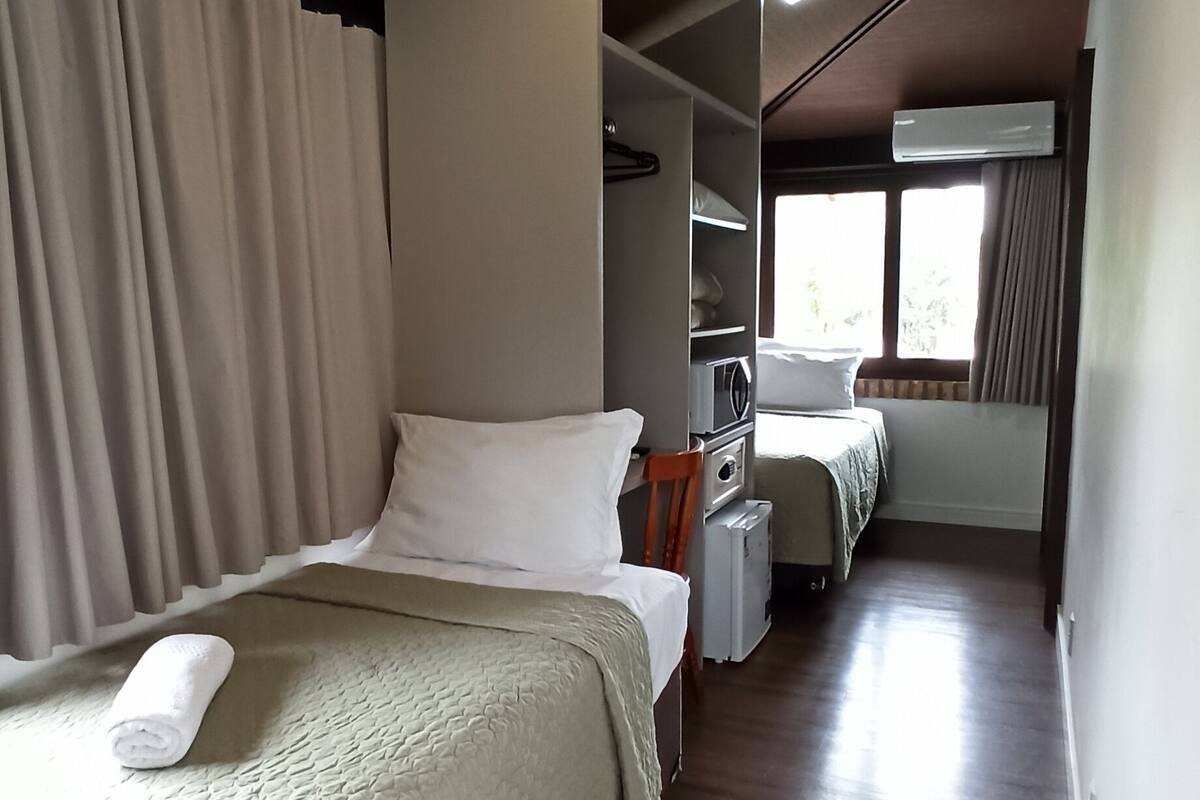 Een hotelkamer met twee bedden, een kledingkast, een bureau en een raam met gordijnen.