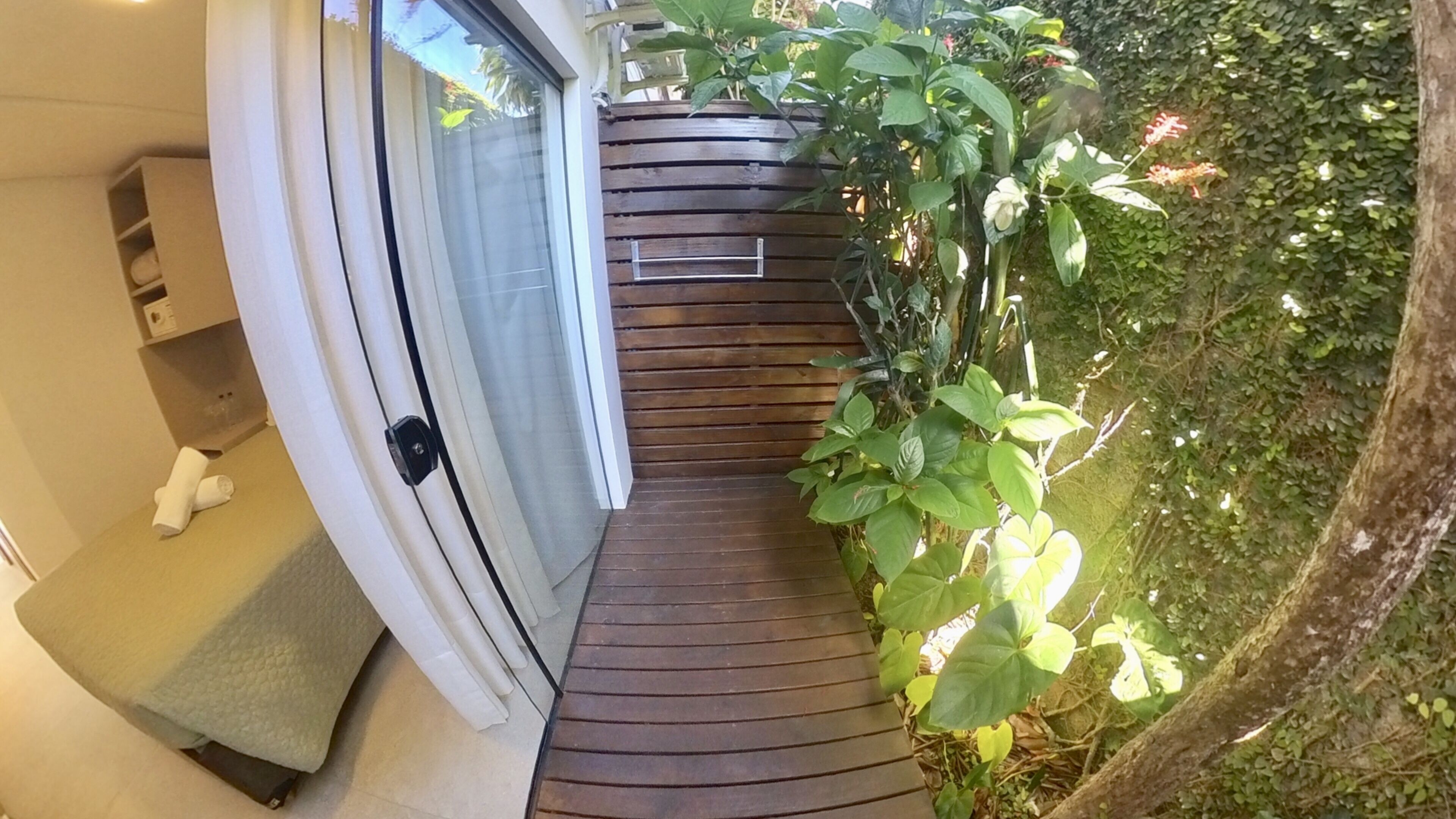 Una terraza de madera con un banco, un ventanal corredero y un pequeño estante con objetos.