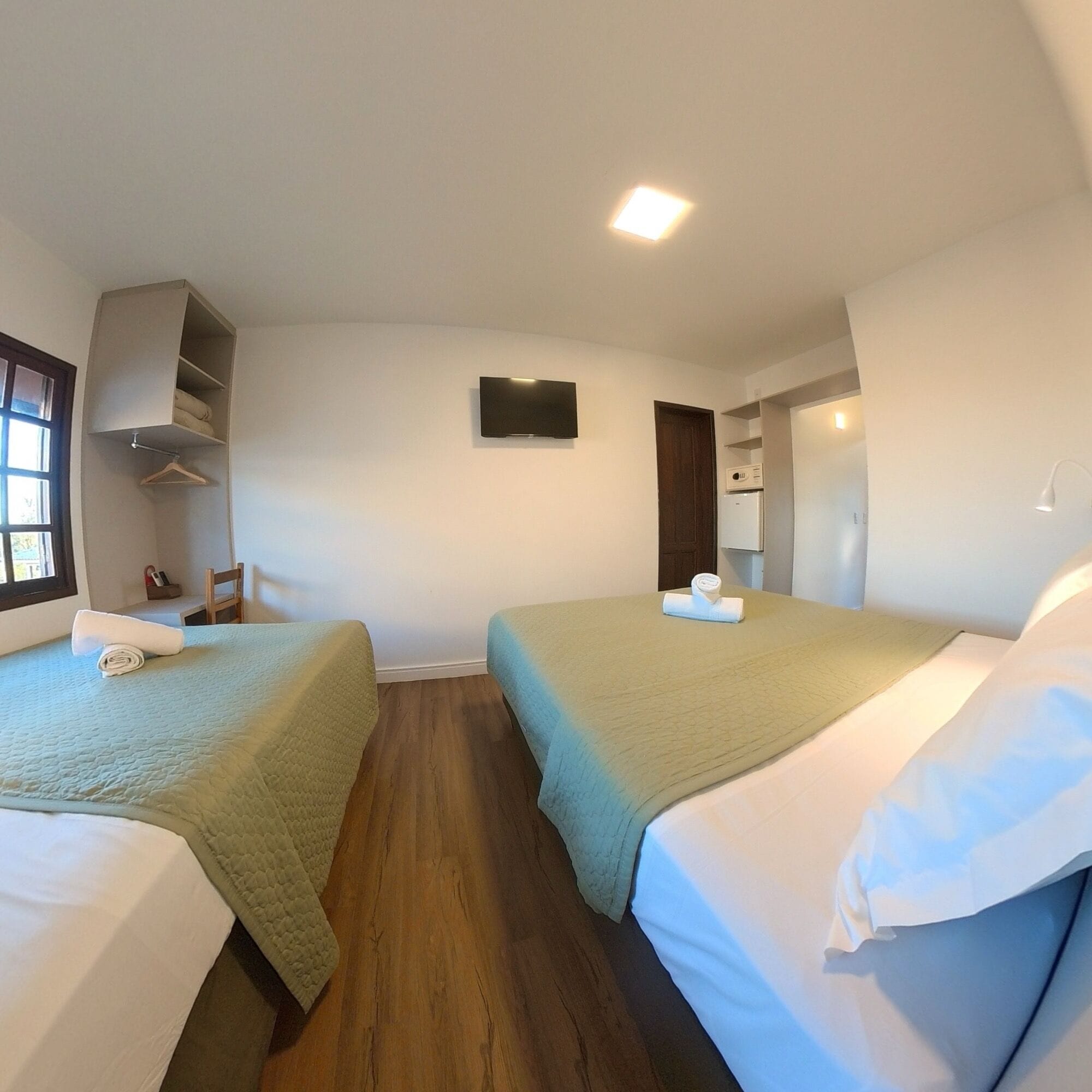 A hotel room with two beds, a TV, a wardrobe, and a small kitchenette.