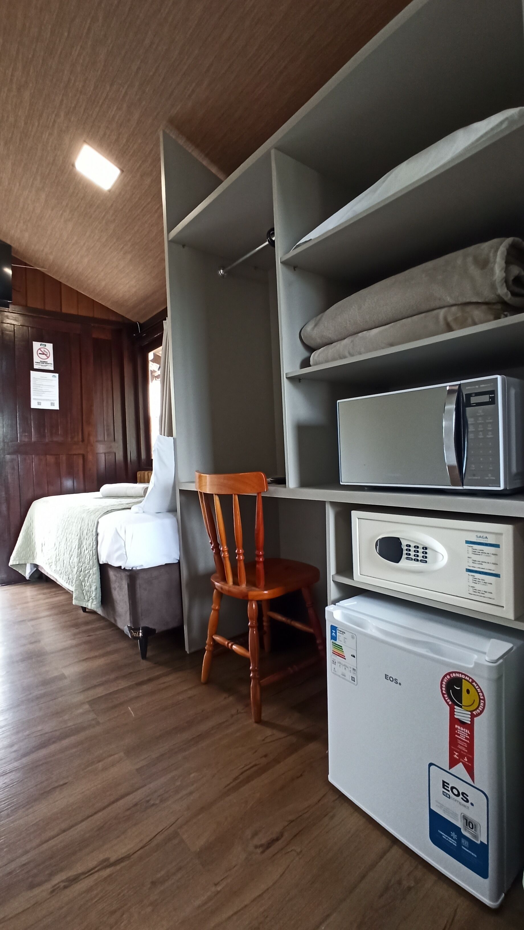 A hotel room with a bed, a chair, a microwave, and a refrigerator.