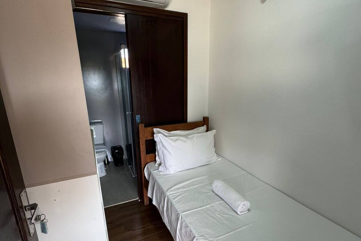 Een kleine, schone kamer met een enkel bed, een houten deur en een witte airconditioningunit aan de muur.