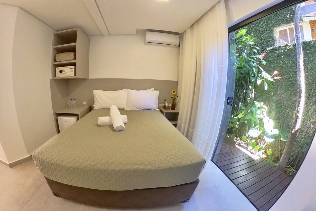 Een slaapkamer met een bed, nachtkastje, ingebouwde plank en uitzicht op groen door een schuifdeur.