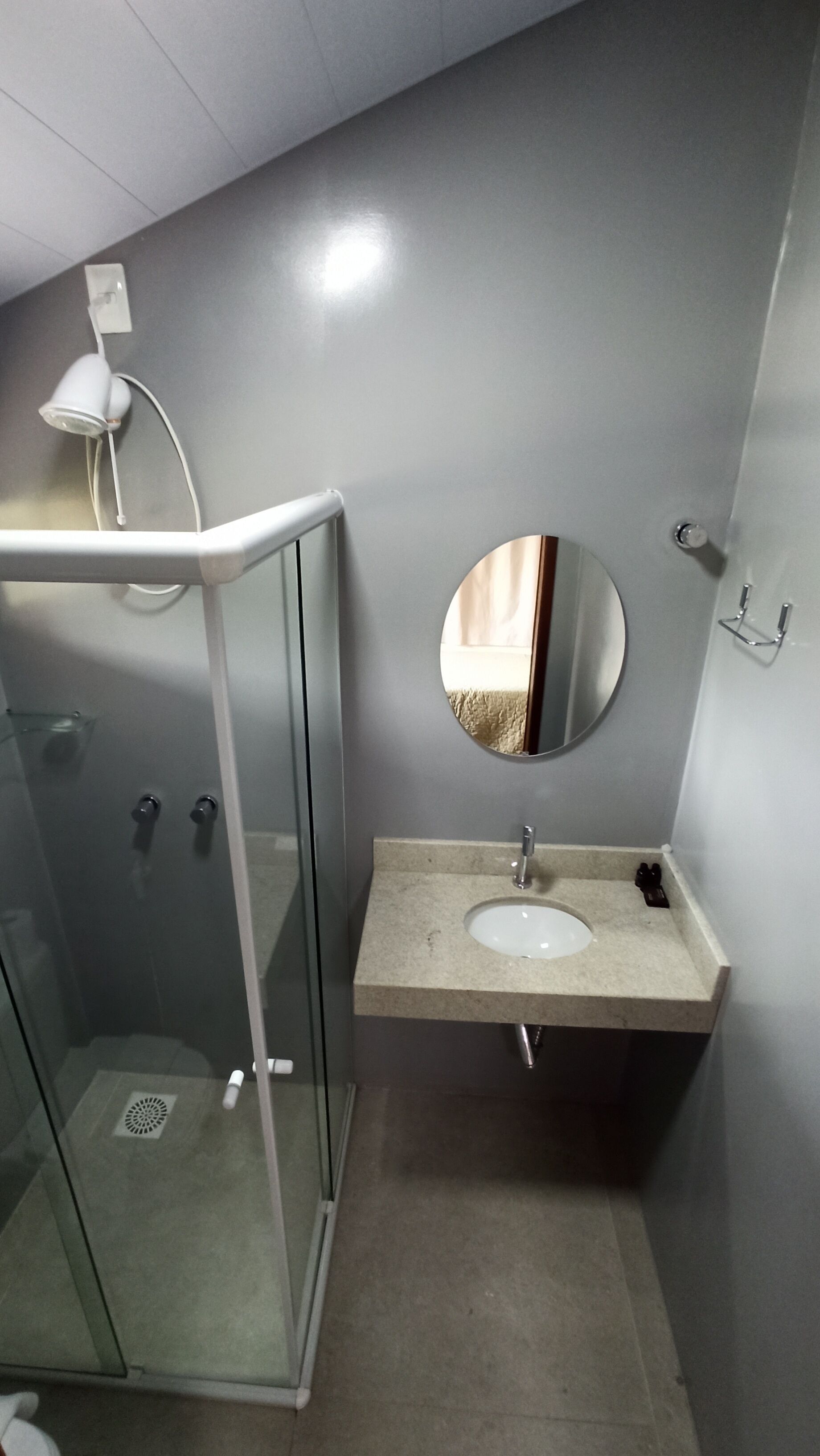 Un baño con cabina de ducha de vidrio, lavabo con espejo y un perchero para toallas.