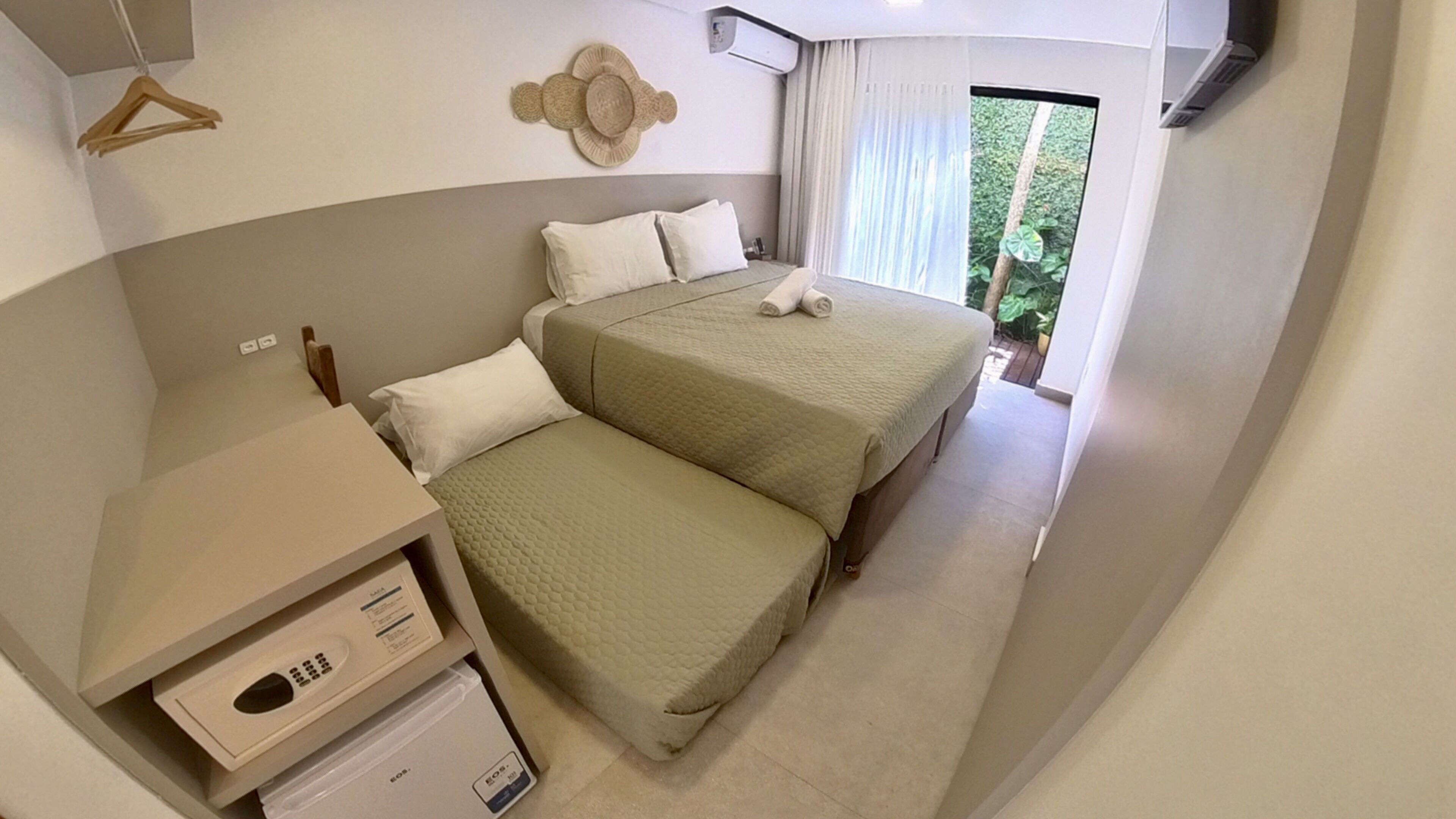 Quarto de hotel com duas camas, uma pequena escrivaninha e uma janela com vista para o verde.