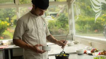 Un chef prépare des plats dans une cuisine donnant sur un paysage verdoyant.